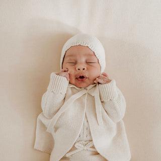 Baby wearing knitted bonnet and matching outfit