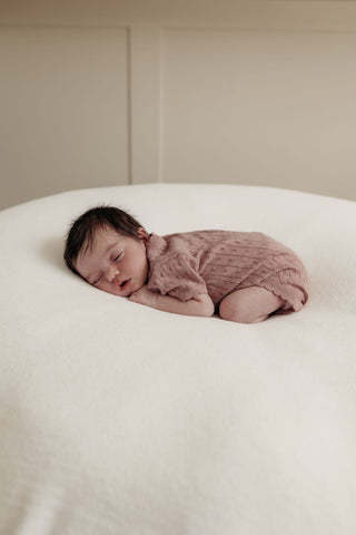 Baby sleeping on beanbag wearing knitted pink bodysuit