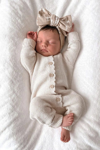 Sleeping Baby wearing a knitted baby romper wearing a bow headband