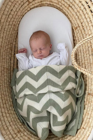 Baby in a basket tucked in with an Organic Cotton Sage Chevron Knit Baby Blanket.