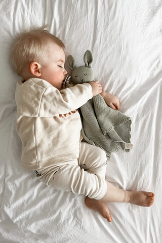 Sleeping Baby lying on a bed cuddling Sage Organic Cotton Isla Bunny Comforter