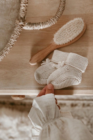Knitted baby bow booties on a dresser next to a baby hairbrush and basket