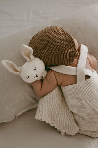 Baby cuddling Organic Cotton Isla Bunny Comforter wearing a knitted bonnet and dungarees