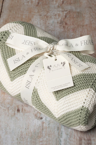 Organic Cotton Sage Chevron Knit Baby Blanket tied with a ribbon on a wooden backdrop