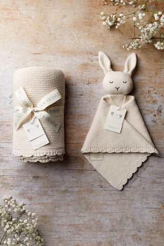Gift Bundle containing an Oat Organic Cotton Baby Blanket tied with a ribbon and an Organic Cotton Bunny Comforter Gift Bundle on a wooden backdrop with gypsophilia in corners