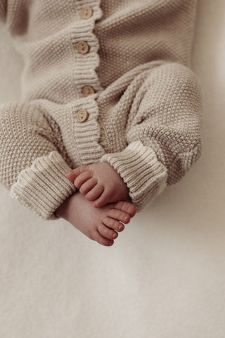 baby feet wearing knitted beige romper with cream cuffs