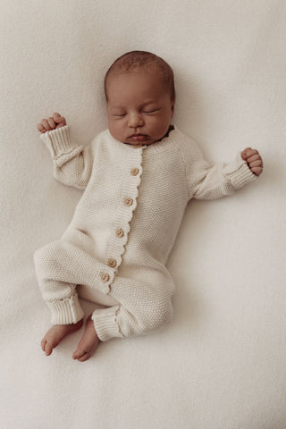Sleeping newborn baby wearing knitted beige romper