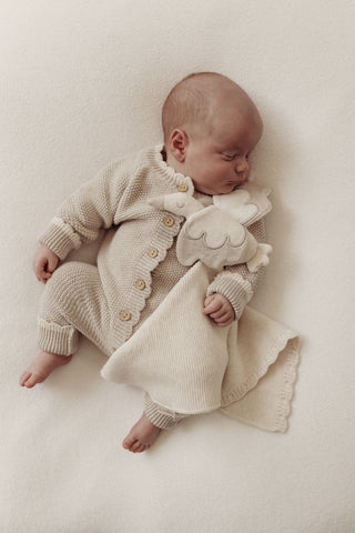 Sleeping baby with cream and grey knitted romper and stork comforter