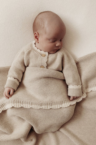 Sleeping baby wearing knitted beige romper with a knitted scallop edge baby blanket