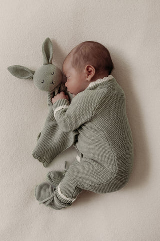 Sleeping baby wearing sage green knitted romper cuddling sage green knitted bunny comforter
