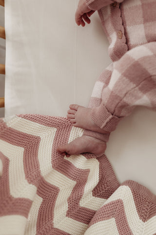 baby feet wearing checkered knit romper, with a pink and cream chevron stripe blanket