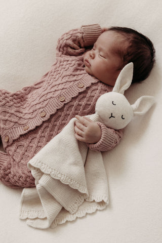 Newborn baby wearing pink cable knit romper cuddling knitted bunny comforter