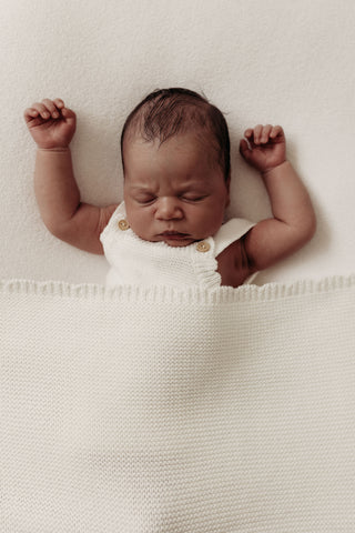 Sleeping baby wearing knitted white romper with white blanket