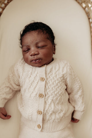 Sleeping baby in moses basket wearing cable knit cardigan