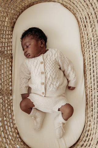 Sleeping baby in moses basket wearing oat knit outfit
