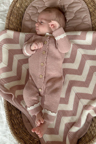 Baby in Basket wearing a Knitted Rose Pink Romper lying on a Chevron Stripe Knitted Baby Blanket in Rose and Cream