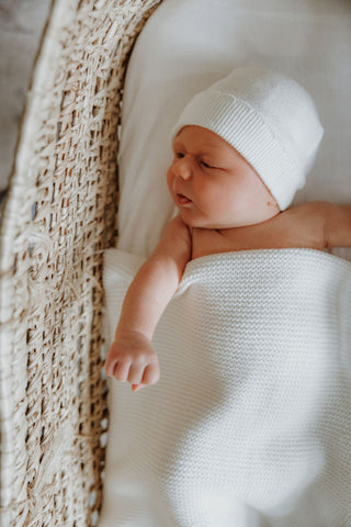 Newborn baby in moses basket with a knitted white hat and blanket
