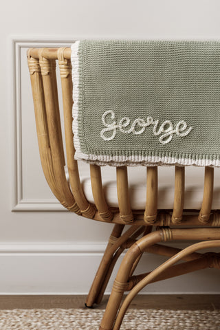 Embroidered 'George' knitted sage baby blanket over a bamboo cot