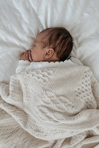 Sleeping baby with dummy and cable knit blanket