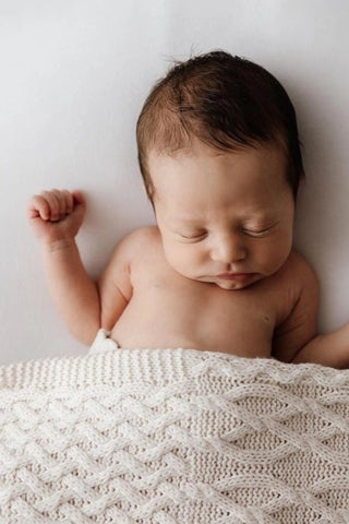 Sleeping baby with beige cable knit blanket
