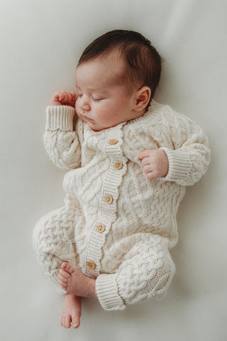 Napping baby wearing the oat coloured organic cotton baby romper in unique cable-knit design. The breathable knit is visible