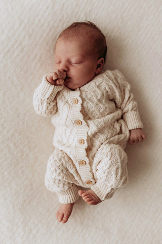 Baby napping whilst wearing the oat coloured baby romper in unique cable knit pattern with breathable knit