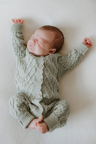 Newborn baby stretching wearing a sage green cable knit romper