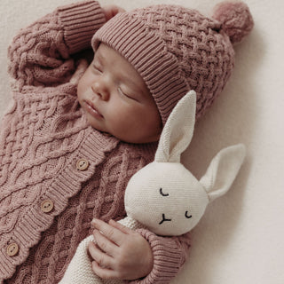 sleeping baby in cosy pink cable knitted outfit cuddling a knitted bunny