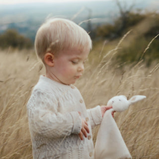 Baby walking through long grass holding bunny comforter
