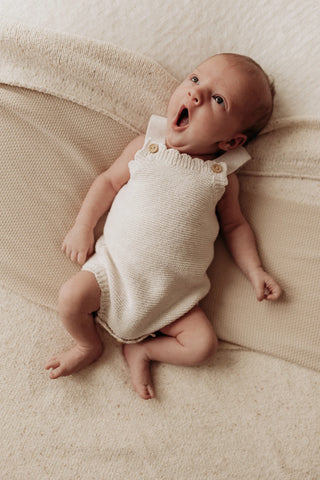 Baby yawning lying on a blanket wearing a knitted romper one piece