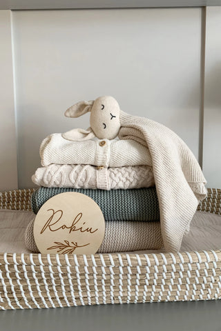 Organic Cotton Bunny Comforter lying on a pile of folded baby knitwear with a baby name plaque