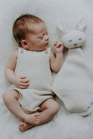 Sleeping baby wearing a knitted baby romper with a knitted bunny comforter