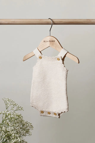 Knitted Baby Romper hanging on a wooden rail on an Isla & Fraser hanger with flowers