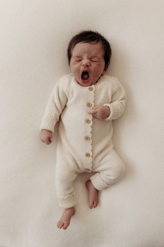 Yawning baby wearing knitted cream romper