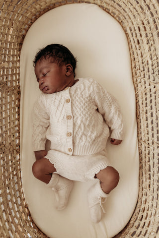 sleeping baby in moses basket wearing knitted oat set
