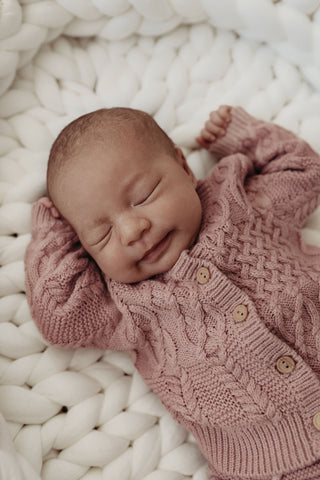 Sleeping baby wearing pink cable knit cardigan lying in a knitted baby nest