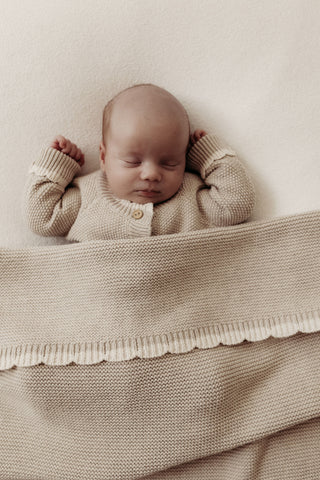 Sleeping baby wearing knitted beige romper with a knitted scallop edge baby blanket