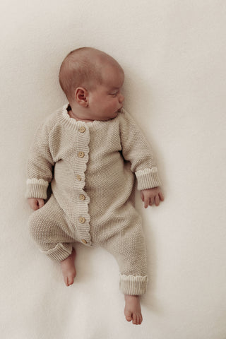 Sleeping baby wearing knitted beige romper with cream cuffs