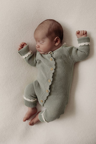 sleeping baby wearing knitted sage green baby romper with cream cuffs