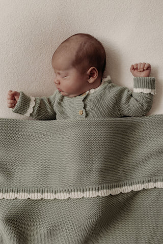Sleeping baby wearing sage green knitted romper with sage green knitted baby blanket