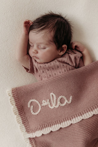 Sleeping baby wearing pink knitted bodysuit with matching knitted blanket with name embroidered in cream: Orla