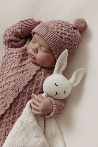 Sleeping baby wearing cable knit hat and romper cuddling bunny comforter