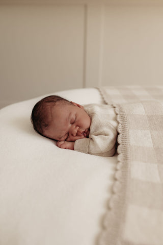 Sleeping newborn on beanbag covered with a grey gingham check blanket with scalloped edges