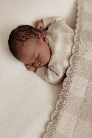 Sleeping newborn on beanbag covered with a grey gingham check blanket with scalloped edges