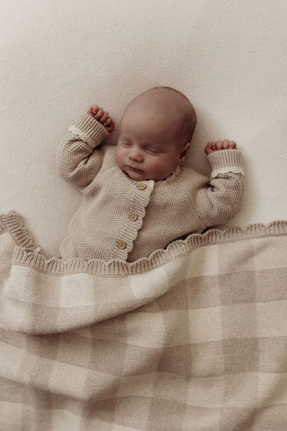 Sleeping newborn wearing a grey knitted romper covered with a grey gingham check blanket with scalloped edges