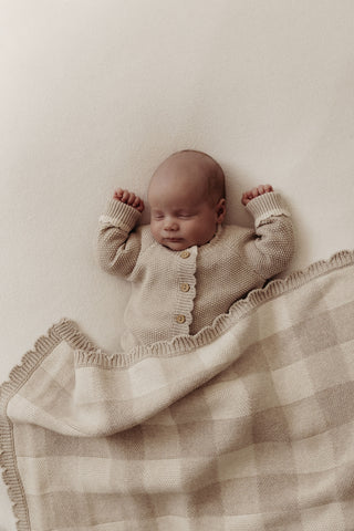 Baby wearing grey knitted romper with a grey check blanket