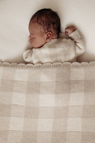 Sleeping newborn on a beanbag covered with a grey gingham check blanket with scalloped edges