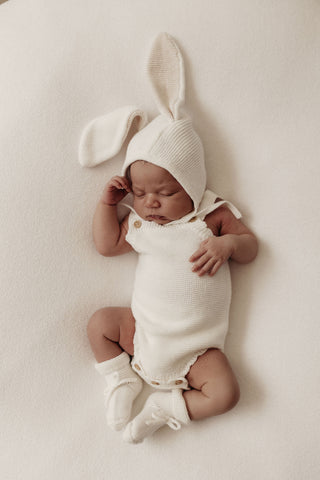 Newborn baby wearing a white bunny ear bonnet, romper and booties