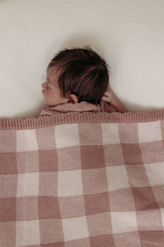 Sleeping baby under a check baby blanket in pink and cream