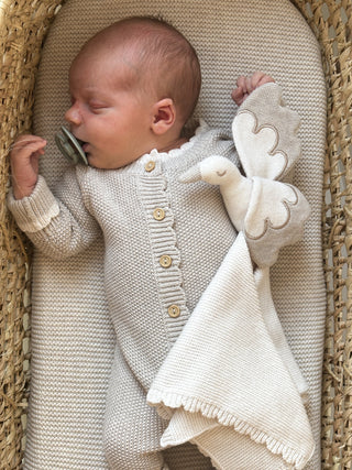 sleeping baby in moses basket wearing knitted romper and cuddling stork comforter